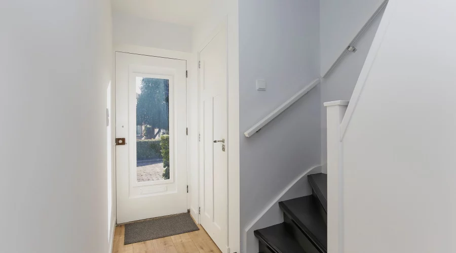 Een gang met een trap die naar een deur leidt. verkoopstyling schiedam, neutrale inrichting, woningfotografie