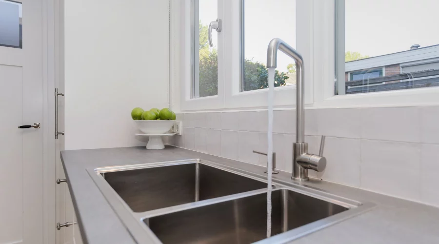 Een roestvrijstalen spoelbak in een keuken met een raam. verkoopstyling schiedam, neutrale inrichting, woningfotografie