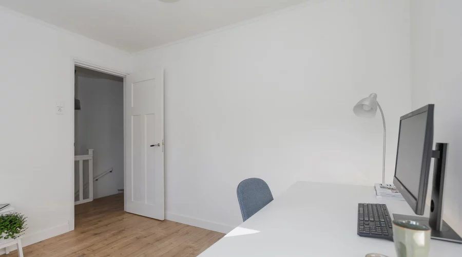 Een witte kamer met een computerbureau en stoel. verkoopstyling schiedam, neutrale inrichting, woningfotografie