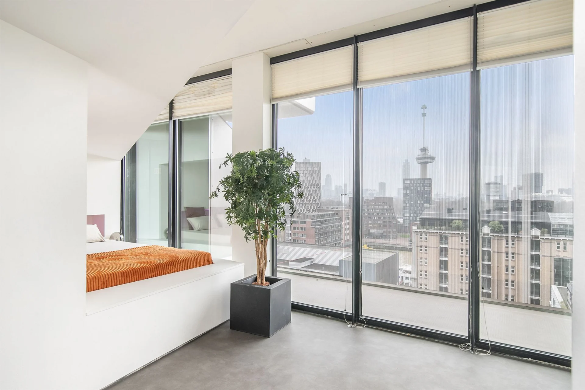 Een slaapkamer met grote ramen en uitzicht over de stad.